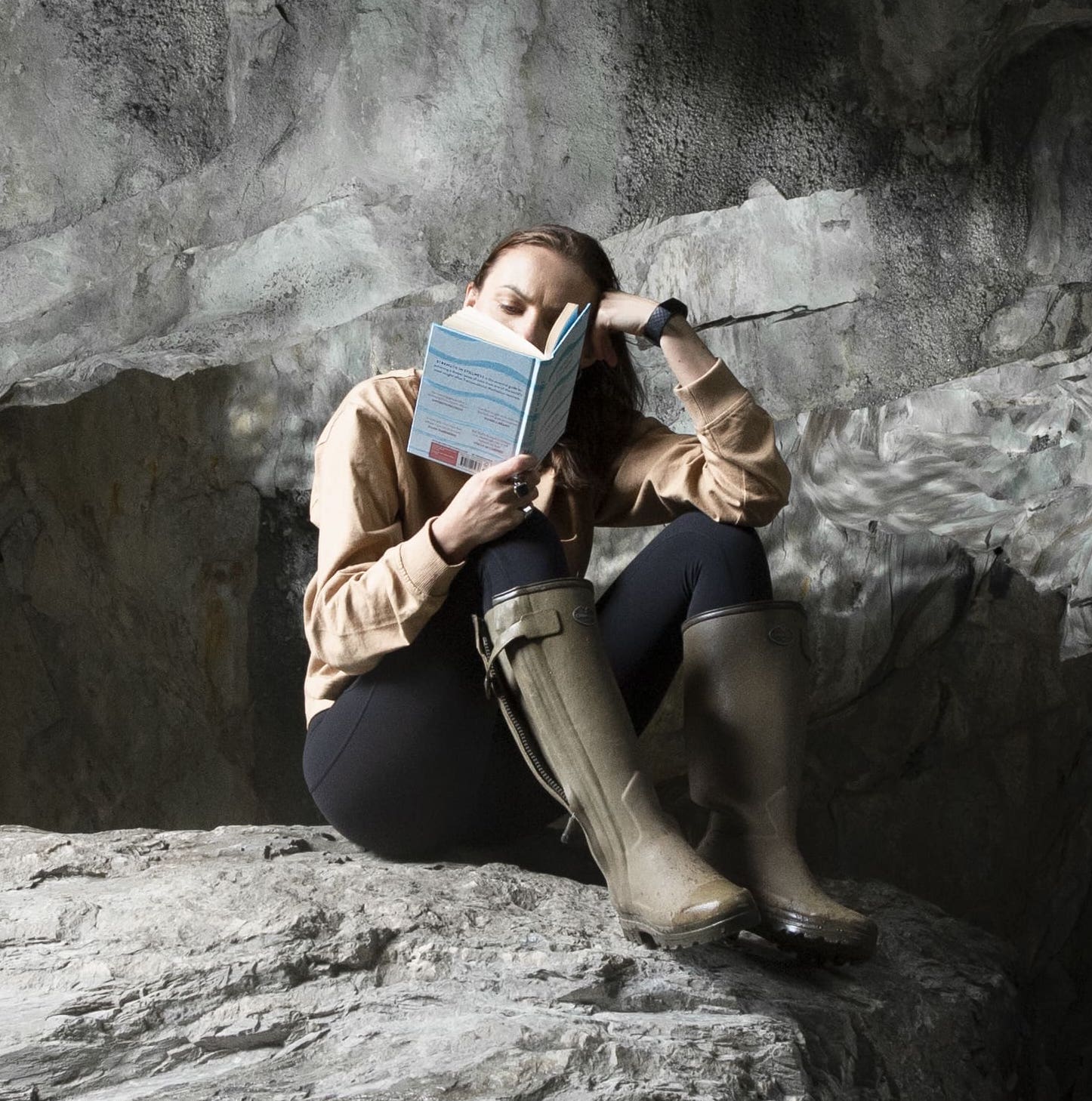 Headshot of Liz reading a book sat on a rock