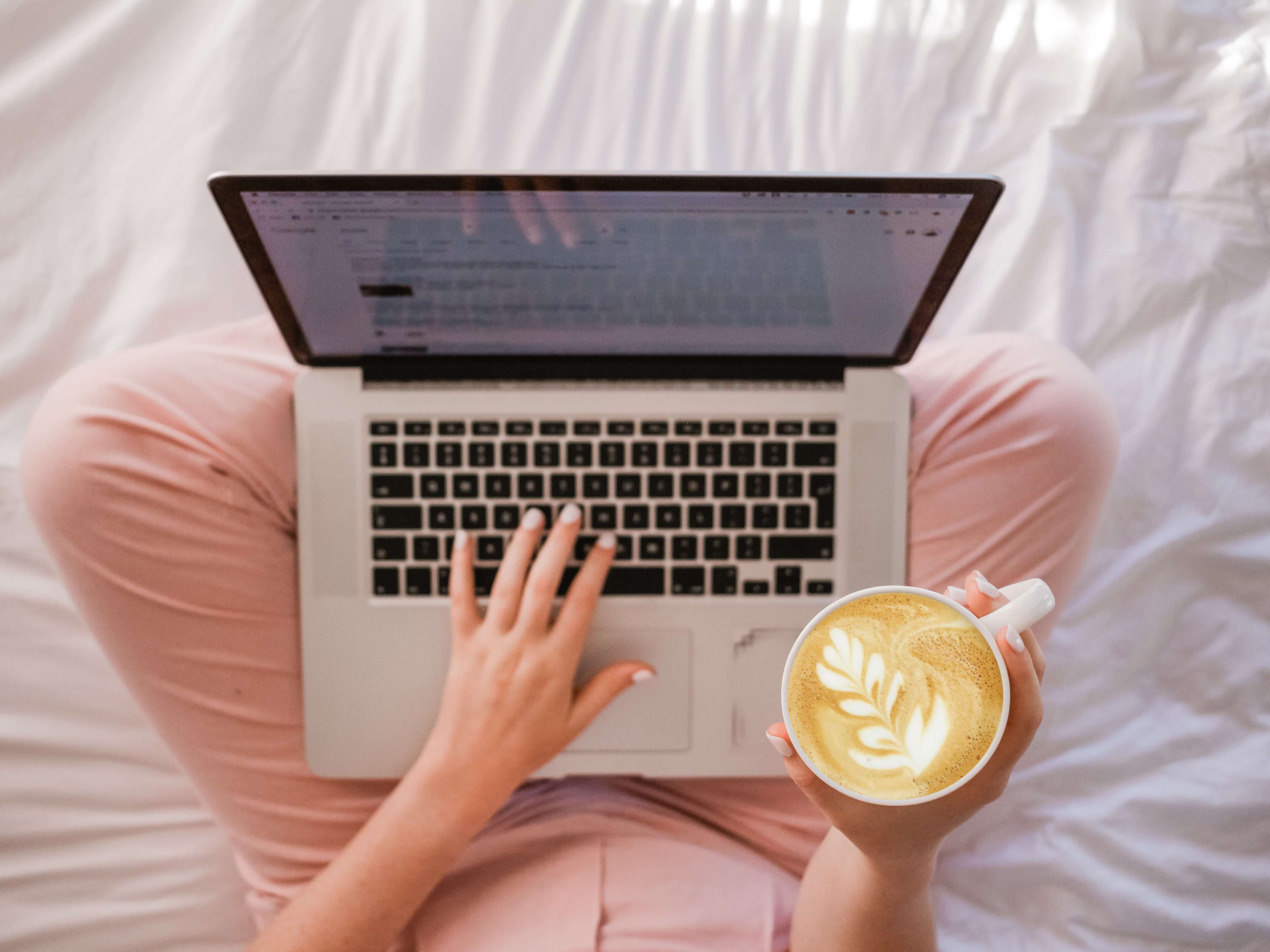 A laptop on a ladies lap who is drinking a latte